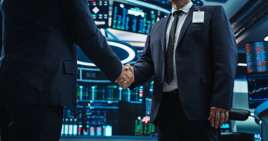 Two Anonymous Stock Market Traders Shaking Hands in a Technologically Advanced Office with Multiple Computer Screens with Real-Time Financial Data, Economy Forecasts and Predictions