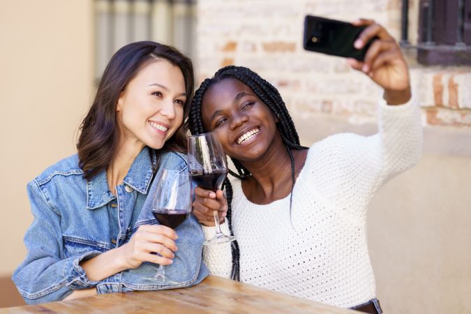 Female friends at an outdoor restaurant with glasses of red wine taking a self portrait