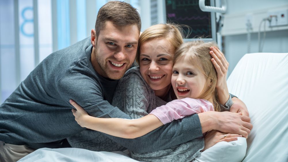 Portrait Shot of Happy Parents Hug Their Cute Little Daughter Lying in the Hospital Bed