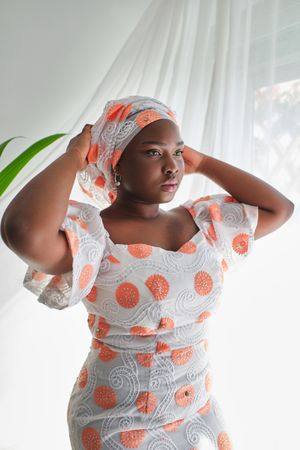 Stylish Black woman in dress standing near window