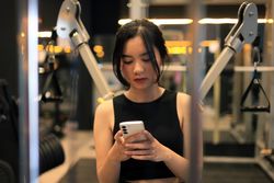 Young Female Sitting on Bench at the Gym with Mobile Phone