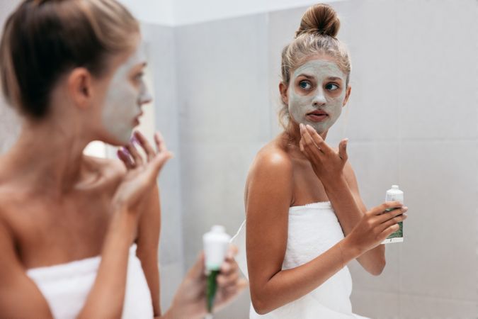 Female in doing beauty treatment on her face skin in front of mirror after bath