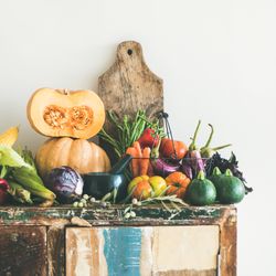 Fresh autumnal produce on kitchen counter, with halved squash and wooden board, square crop