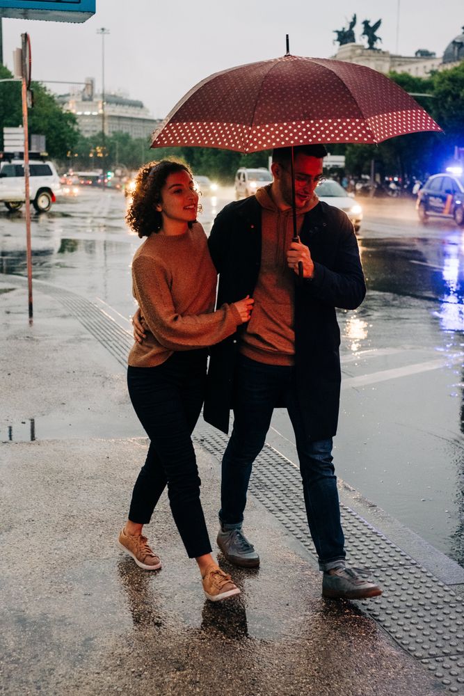 Happy couple with umbrella hugging on wet street