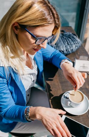 Blonde woman stiring coffee and looking phone