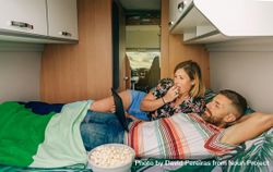 Male and female relaxing on bed in motorhome with popcorn 0KXWM5