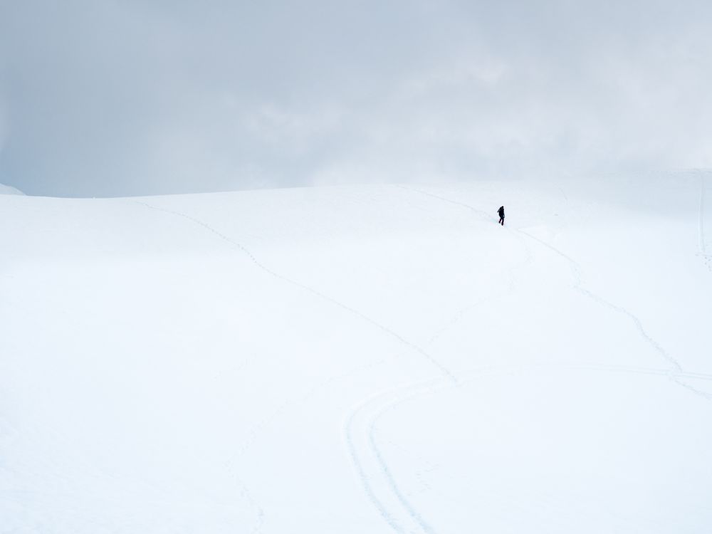 Unrecognizable lonely traveler walking on snowy hill