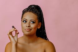 Contemplative Black woman holding lip gloss while looking up