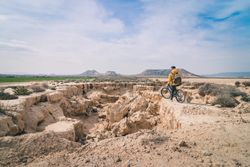 Man with bicycle standing on stone in desert hills