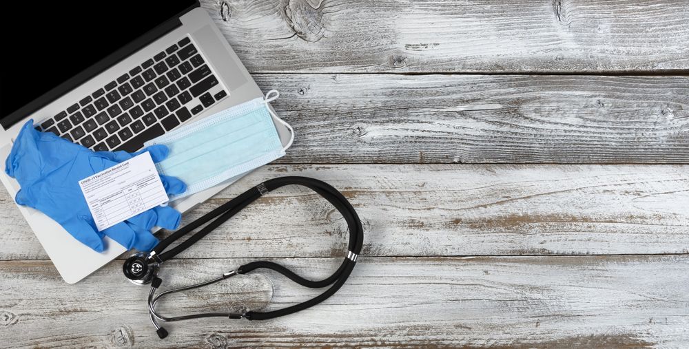 Covid 19 vaccination record card with stethoscope plus laptop and facemask