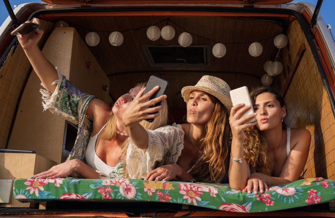 Relaxed girl friends taking selfie comfortable placing on trunk of blue car