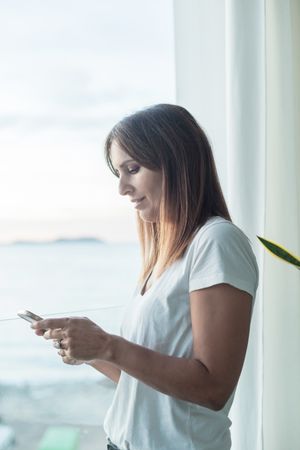 Side view of woman checking phone sitting next to window