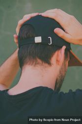 Back view of man with dark cap touching his head bYJaD0