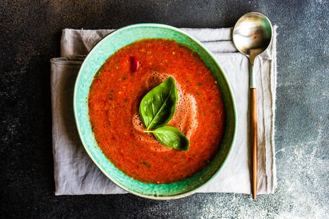 Green bowl of gazpacho soup with basil leaves on napkin