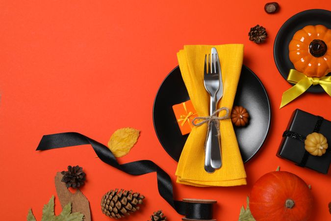 Cutlery on plate, pumpkins and leaves on red background, space for text