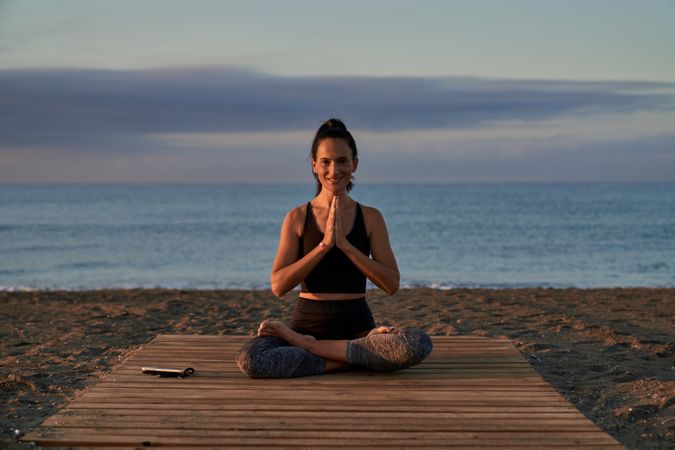 Positive Hispanic woman meditating on shore