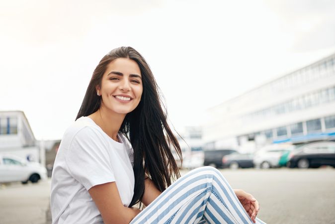 Woman sitting on curb on overcast day and smiling