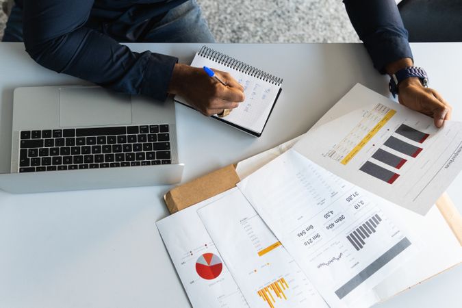 Black guy writing in notepad near laptop in office