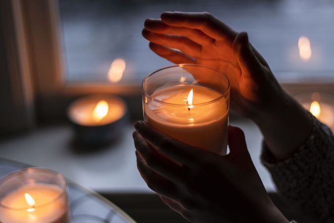Person holding a lit candle in clear glass indoor