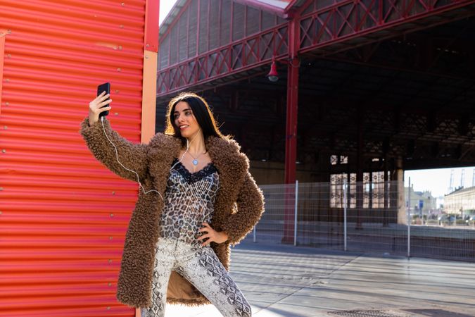 Trendy woman with smartphone near wall