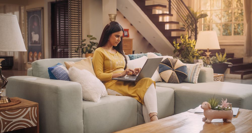 Indian Woman Works Remotely From Home, Seated On A Cozy Sofa With Laptop. Productive and Efficient at Virtual Management.