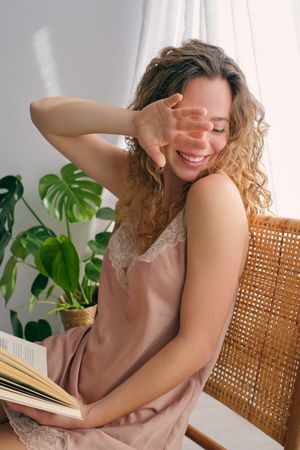 Happy young woman with book sitting on wicker chair