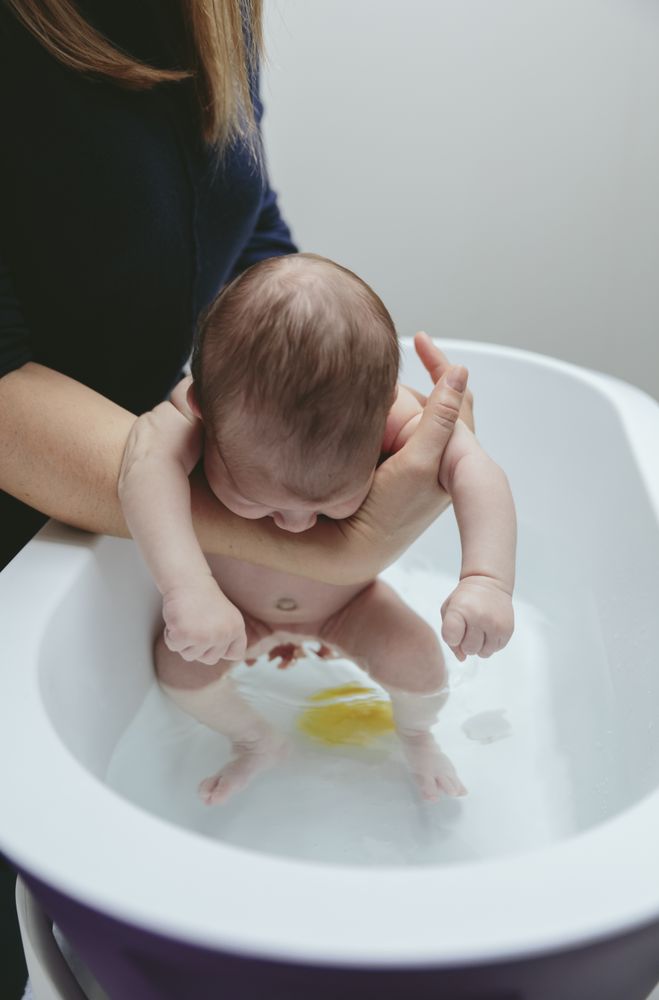 Newborn in the bathtub held by her mother