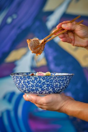 Faceless person eating meat of ramen soup with chopsticks