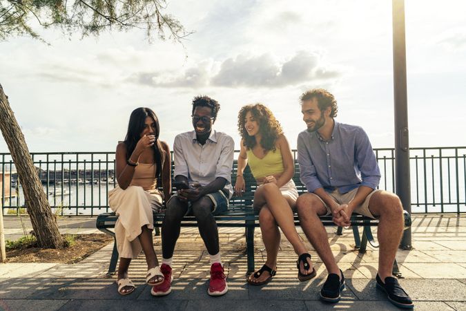 Group of friends laughing with a smartphone on a bench