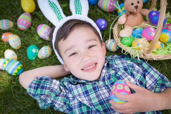 Smiling Boy Outside Wearing Rabbit Ears Playing with Easter Eggs