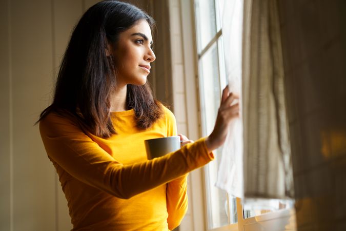 Female gazing out the window with warm beverage