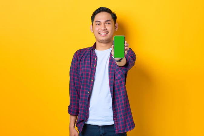Happy Asian man in plaid shirt  holding smartphone with chroma key