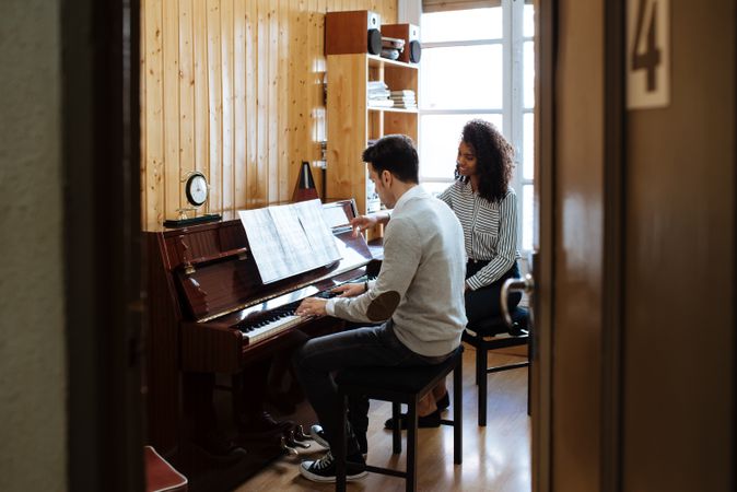 Man playing piano near woman teaching in studio