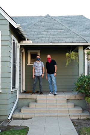 Two men in coronavirus mask standing on front porch