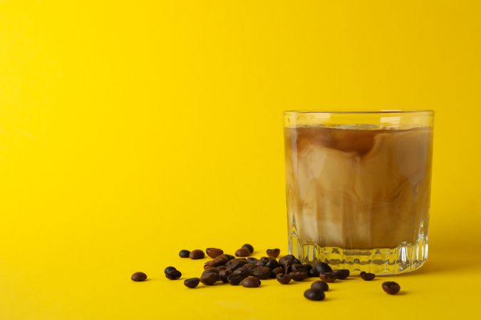 Glass of ice coffee on yellow background. Fresh drink