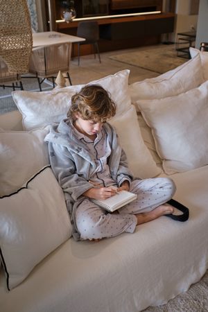 Boy studying and writing information in paper notebook at home