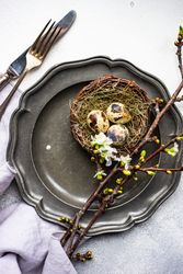 Top view of decorative nest and cherry blossom branch on dark table setting