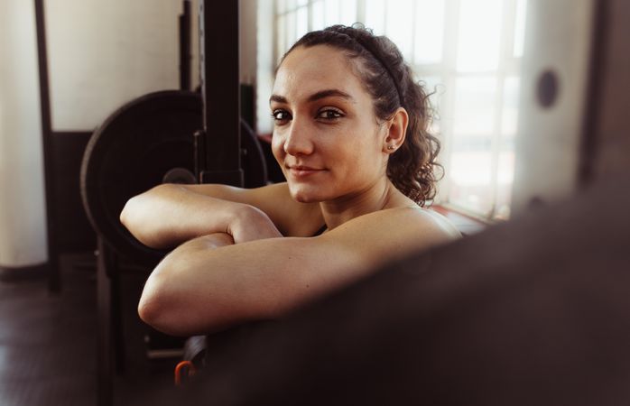 Happy young woman leaning over barbell in fitness center