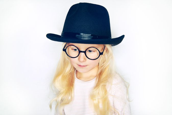Serious blonde girl looking down wearing hat and glasses