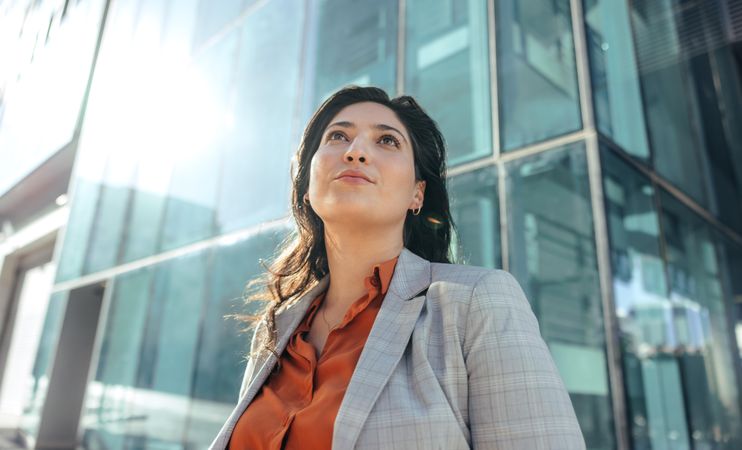 Female entrepreneur looking up thoughtfully while standing in front of a high rise