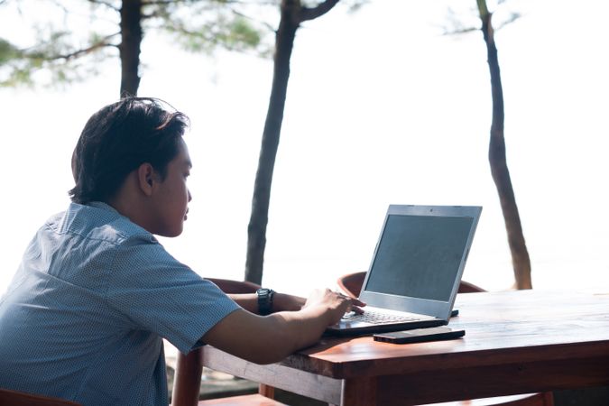 Back View Asian Young businessman work at outdoor with laptop blank screen. Concept of remote and freelance work. Young successful man wearing casual blue cloth.
