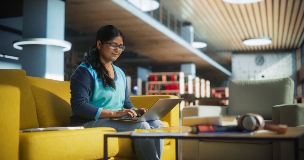 Smart Indian Female Student in Glasses Working on Software Development Assignment in a Quiet Public Library. Young South Asian Woman Using Laptop Computer and Preparing for Examination in College