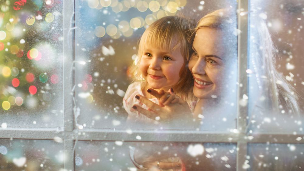 On Christmas Eve Mother and Daughter Looking Through Window with Snowy Effect.