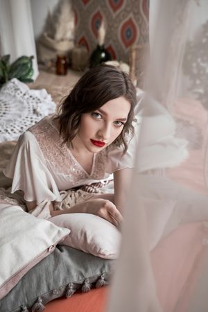 woman with red lips in white dress looking at camera while sitting on floor beside sofa