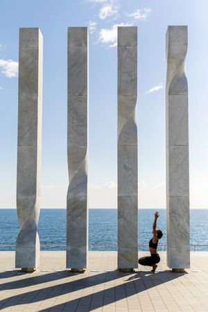 Side view of female stretching up on sculpture by the ocean