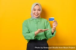 Smiling Muslim woman in headscarf and green blouse presenting her credit card bDzy85