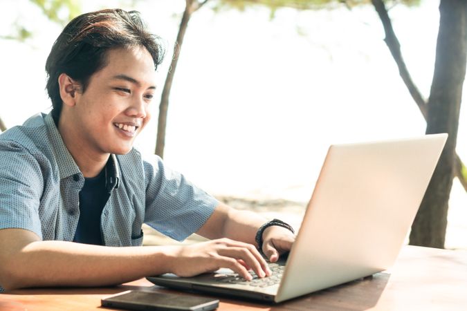 Happy Asian Young businessman work at outdoor with laptop. Concept of remote and freelance work. Young successful man wearing casual blue cloth.