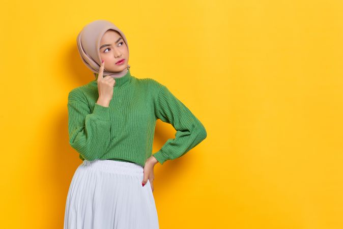Woman in headscarf wondering about something with finger on cheek with copy space