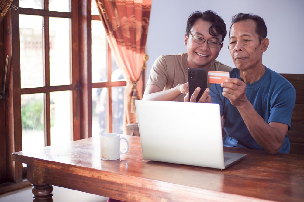 Happy adult son and older father pay online using laptop and credit card