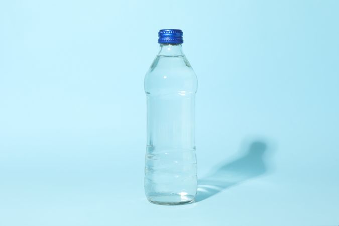 Full water bottle in blue room with shadow, copy space